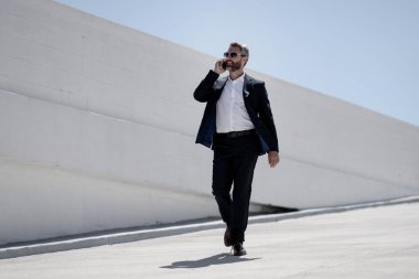 İş adamı dışarıda telefonla konuşuyor. Telefon görüşmesinde başarılı bir adam. İş adamı dışarıyı arıyor. Cep telefonu olan yakışıklı bir iş adamı. Cep telefonundan konuşan kendine güvenen bir adam. Çevrim içi iş