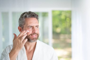 Adam evde güzellik maskesinin keyfini çıkarıyor. Erkek güzellik modeli güzellik için yüz kremi uyguluyor. Erkek için yüz ve gençleştirme. Güzel sabah rutini
