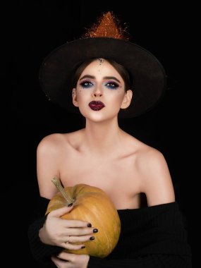 Halloween woman portrait in witch hat with pumpkin. Halloween witch woman portrait in studio. Halloween woman portrait in hat celebrating Halloween party. Woman portrait with horror style makeup