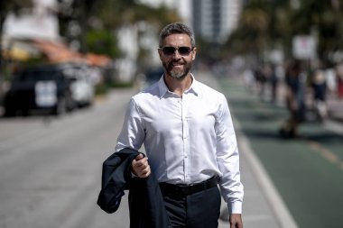 Olgun iş adamı şehirde güvenle yürüyor. Sokakta yürüyen bir iş adamı. Ofise doğru yürüyen yakışıklı bir iş adamı. Açık havada yürüyen kendinden emin bir girişimci.