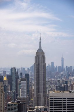 New York şehrinin panoramik bir görüntüsü. Önplanda ikonik Empire State Binası var. Parçalı bulutlu bir gökyüzünün altında modern gökdelenlerin silueti var..