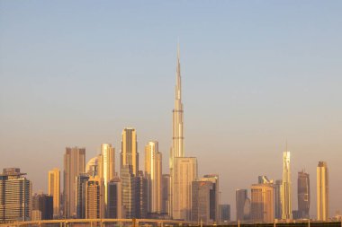 Dubai 'nin gökdelenlerle çevrili, günbatımında berrak bir gökyüzü altında ikonik Burj Halife' yi gösteren bir gökyüzü..