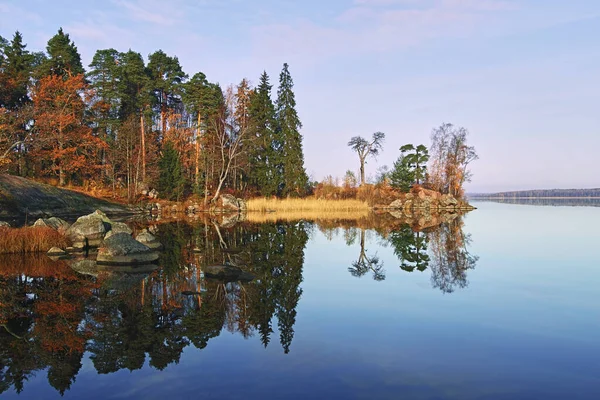 Autumn nature of Northern Europe: cape on lake, sunny day, reflection of forest in water.