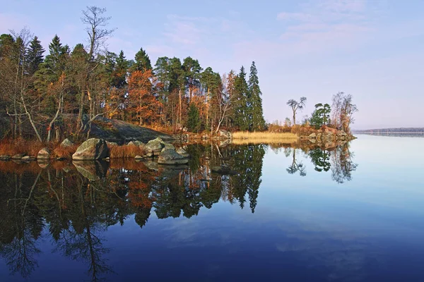 Autumn nature of Northern Europe: cape on lake, sunny day, reflection of forest in water.