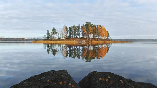 Autumn nature of Northern Europe: island on lake, sunny day, reflection in water.