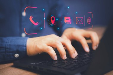 Bilgisayar dizüstü bilgisayar kullanan ve sanal ekran iletişim simgelerine dokunan bir adam (telefon, e-posta, adres, canlı sohbet, harita). Bizimle irtibata geçin ya da müşteri destek hattı bağlantısını kurun.