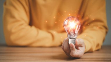 Ahşap bir masanın üzerinde parlayan bir ampul tutan adam, iş problemleri fikirleri çözen ve yaratıcı pazarlama fikirleri icat eden ve yeni şeyler öğrenen adam..