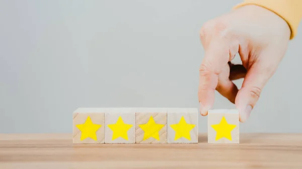Customer's hand selects a star icon on a wooden cube block with 5 Star Satisfaction. Best great business services rate the customer experience. Satisfaction Survey Concept.