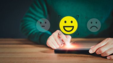 Man hand using a mobile phone with popup smile face icon for feedback review satisfaction service and testimonial. Customer service experience assessment and business satisfaction survey.
