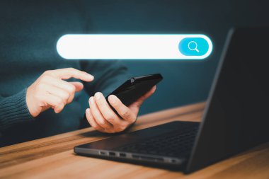 Yetişkin bir adam masanın üstünde cep telefonu ve bilgisayar laptopuyla çalışıyor. Boş arama çubuğu ile internet veri bilgileri taranıyor. Arama motoru optimizasyonu SEO ağ konsepti.