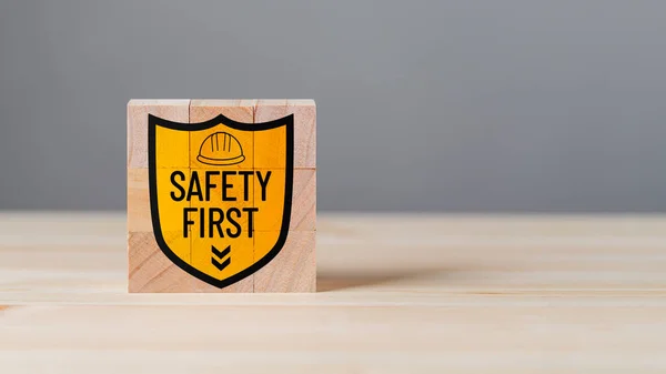 Wooden cubes on wood table background. Concept of safety banner, caution work hazards, danger surveillance, safety first symbol, work safety, zero accident, worker safety awareness at workplace.