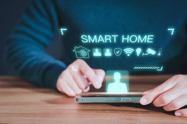 Yetişkin adam teknolojiyi kontrol ediyor. Yapay zeka akıllı ev aletleri, oturma odasında uygulaması açık olan akıllı bir telefon kullanıyor. Çok akıllı ev otomasyon uygulaması kavramı.