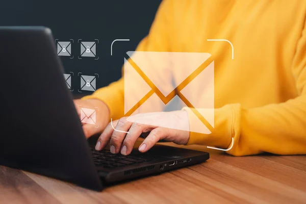 Concept of Email marketing, send e-mail or news letter, online working internet network. Man hand using computer laptop typing on keyboard and surfing the internet on office table with email icon.