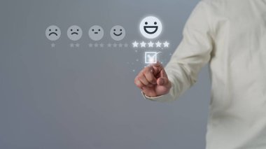Değerlendirme müşteri hizmetleri ve geri bildirim konsepti. Adam, mutlu gülümseme yüz simgesine sanal ekrana dokunuyor ve hizmette tatmin olmak için beş yıldız alıyor. Düşünce oranı çok etkileyici..