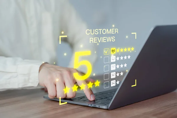 Customer hand using a computer laptop with pop up smiley face and five star icon for assessment feedback review satisfaction and testimonial. Customer service experience and business satisfaction survey.