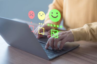 Müşteri, geri bildirim memnuniyeti görüşünü değerlendirmek ve ifade vermek için gülen surat ikonunda sanal ekranlı bir dizüstü bilgisayar kullanır. Müşteri hizmetleri deneyimi ve iş memnuniyeti anketi.