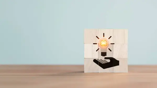 Wooden cube block with hand holding illuminated light bulb icon. Concept of new ideas with innovation, creative idea, new business plan, motivation, innovation, inspiration. Energy saving light bulb.