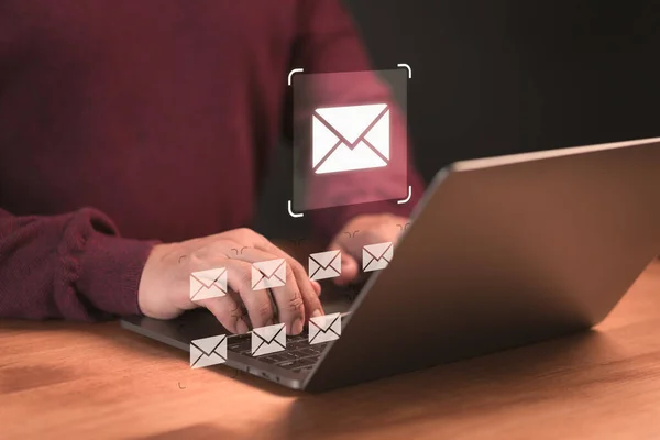 Concept of Email marketing, send e-mail or news letter, online working internet network. Male hand using a computer laptop typing on keyboard and surfing the internet on office table with email icon.