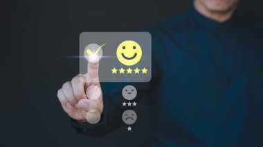 Müşteri eli, hizmette tatmin olmak için mutlu gülümseme simgesine sanal ekrana dokunuyor. Değerlendirme kavramı beyan müşteri hizmetleri ve geri bildirim, görüş derecesi çok etkileyici.