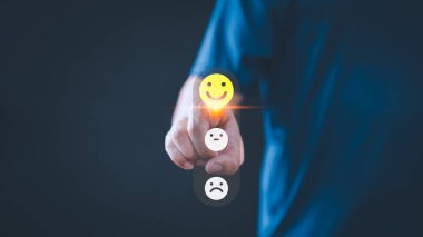 Kişi, çevrimiçi geri bildirim sisteminde müşteri memnuniyetini, gözden geçirmesini ve olumlu kullanıcı deneyimini, karar alma mekanizmasını sembolize eden üç emoji seçeneğini içeren bir geri bildirim boyutundan mutlu yüz simgesi seçer..