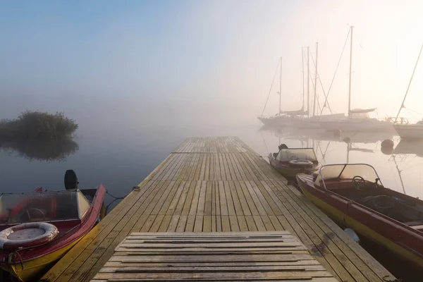 雾蒙蒙的早晨 在小河港口 停泊着帆船和木桥上的汽船 由于雾蒙蒙的背景 显得有些模糊 — 图库照片