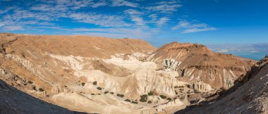 Musevi Çölü 'ndeki panoramik mucizevi hava manzarası, bulutlar ve mavi gökyüzü, sıradışı taş kanyon, antik dağları çevreleyen ve uzak mesafedeki Ölü Deniz 