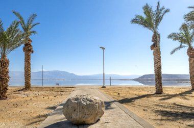 Ölü Deniz. Ölü Deniz 'in tuzlu kıyılarında yaya geçidi ve hurma ağaçları, tatil beldesi ve eski yüzme alanı, kışın güneşli bir gün, İsrail