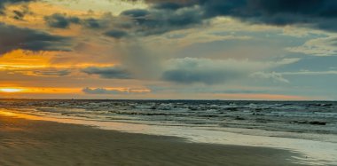 Baltık Denizi 'nin kıyı manzarası. Su ufkunun üstünde renkli bulutlar ve gün batımında güzel güneş ışığı.