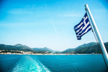 Yunanistan 'ın ulusal bayrağı Yunan ada manzaralarının arka planında bir feribotta ve deniz suyundaki feribotun izini taşıyor.