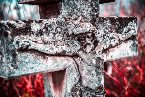 Old stone statue of Jesus crucified on the cross on the tombstone in the cemetery in Ukraine
