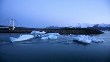 Buzdağı parçaları İzlanda 'daki ünlü Jokulsarlon buz gölünün körfezindeki bir köprünün altında okyanusa doğru yüzer. (Küresel ısınma, sera etkisi - kavram)