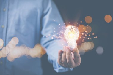 İş adamı ampulü ve dişliyi içeride tutuyor. Yaratıcı yeni fikirler ve fotokopi alanı siyah arka planlı iş için ilham kaynağı. Yenilik ve teknoloji kavramı.