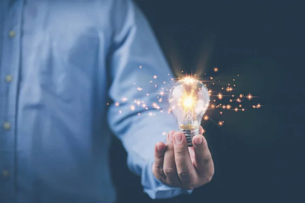 Inspiration for new ideas and innovation to the future. Businessman holding a lightbulb glowing on hand with copy space on black background. Idea, Innovation, and Inspiration concepts.