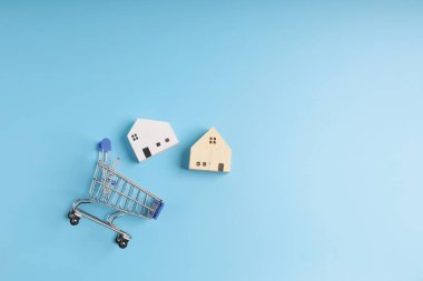 Üst manzara, düz bir alışveriş arabası, üzerinde küçük ahşap evler ve fotokopi alanı olan mavi bir arka plan. Geleceğe yatırım yapmak için para biriktiriyorum..