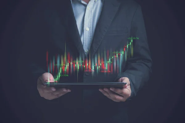 Business growth, progress, success. Investment, financial, business concept. Businessman wearing a black suit holding a tablet in hand with a virtual growth chart for investing in stocks for profit.