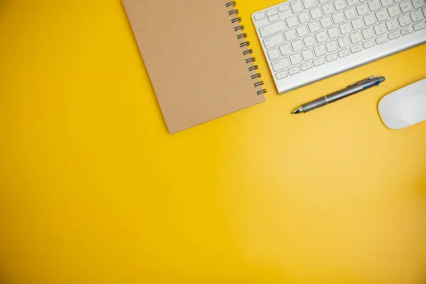 The home office with a pen, and notebook on a yellow table with copy space. Top view, flat lay minimal yellow desk concept. Workspace desk with keyboard on yellow background.