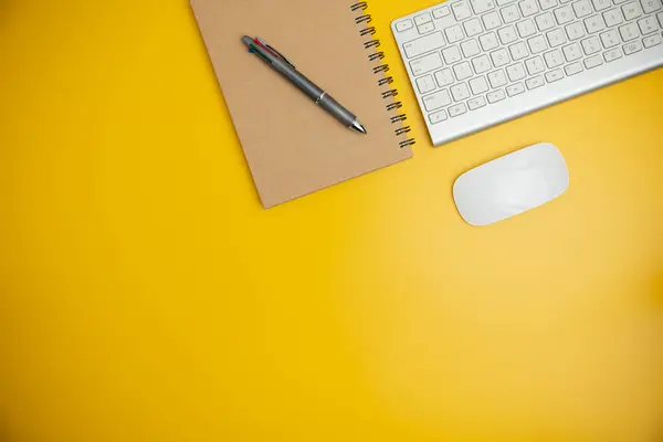 The home office with a pen, and notebook with a mouse on a yellow table with copy space. Top view, flat lay minimal yellow desk concept. Workspace desk with keyboard on yellow background.