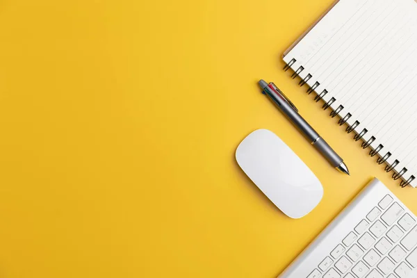 The home office with a pen, and notebook with a mouse on a yellow table with copy space. Top view, flat lay minimal yellow desk concept. Workspace desk with keyboard on yellow background.