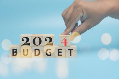 Yeni yıl iş planlama bütçesi ve 2024 tahsisi. 2024 'ü bütçeyle birlikte tahta küplere kopyalama alanı koyan adamın eli. Gelecek yıl için bütçe planlaması, yatırım, yeni iş konsepti.