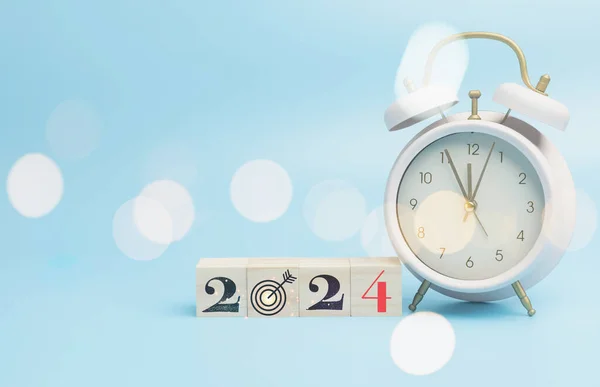 New year 2024 on wood block with vintage a pink alarm clock, copy space blue background. Countdown to new year startup planning financial, budget, set goal challenge for success to the future.