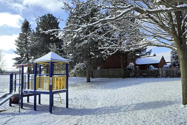 Kids\' play area equipment is covered with snow and trees in the background