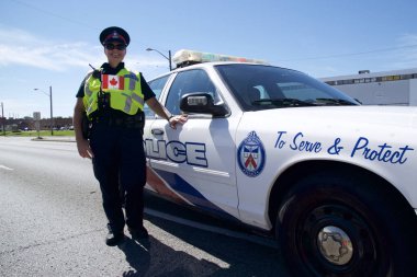 Toronto, Ontario, Canada - 01/07/2019: Police officer  standing beside the police car and looking at camera clipart