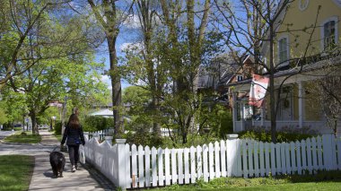 Beyaz çitli bir evde köpek yavrusuyla yürüyen bir kadın.
