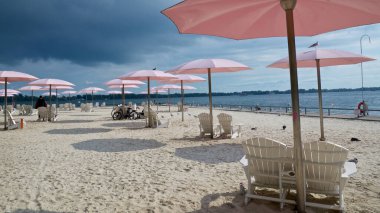 Plajda bulutlu bir gökyüzü Pembe plaj şemsiyeleri ve Adirondack sandalyeleriyle
