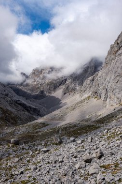 Kordillera Cantbrica, picos da europa, Leon, asturias, İspanya 'da yaz boyunca bulutlarla birlikte güneşli bir günde yürüyüş patikası olan büyük, güzel, gri bir dağ sırası.