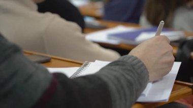 Bir öğrenci üniversitedeki bir konferansta notlar alıyor. Derste not alan bir öğrencinin eli.