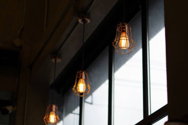 Klasik esinlenilmiş ampullerle kırsal-modern endüstriyel aydınlatma donanımları çelik, cam ve ahşap elementlerle minimalist bir iç mekanda karamsar, atmosferik bir ortam yaratıyor..