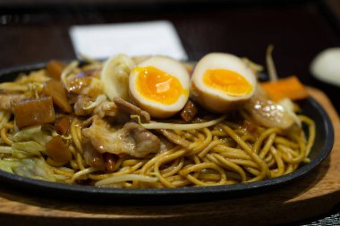 Steaming bowl of savory Japanese udon or ramen noodle soup with slices of soft-boiled egg,tender pork,fresh green onions,and other savory garnishes. clipart