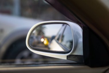 Arka planda yolu, trafiği ve kentsel manzarayı yansıtan modern bir arabanın yan dikiz aynasının yakın görüntüsü.