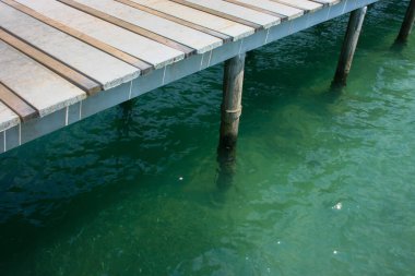 Huzurlu ahşap iskele ya da sakin yeşil bir göl üzerinde huzur içinde yüzen iskele. Etrafı bereketli doğal manzarayla çevrili. Su durgun ve berrak. Tahta yapıyı ve çevreyi yansıtıyor..